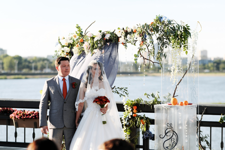 Newlyweds at a wedding arch on the background of a river and a cityの写真素材