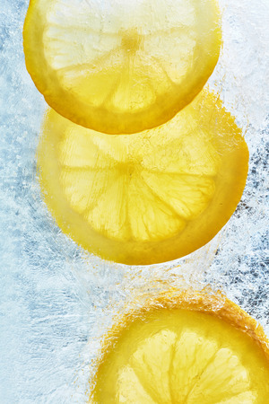 Lemon on the ice. Refreshing summer background of citrus. Yellow lemons and ice photo from above.の写真素材