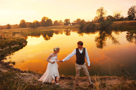 Bride and groom posing against a lake in the red sunsetの写真素材