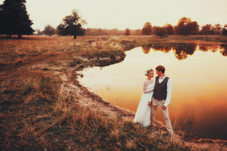 The groom and the bride posing in the evening against the background of the lake in the red sunset.の写真素材