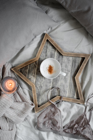A cup of coffee and a candle in a Scandinavian wooden tray in a cozy bed with a blanket.  top view.の写真素材
