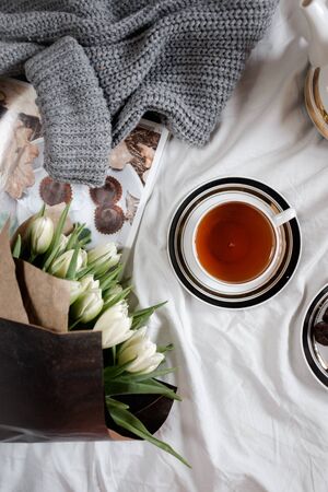 A cozy photo. Top view of a cup of tea and a bouquet of white tulips in black paperの写真素材