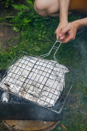 Man fry fish in a foil on a grill in the open airの写真素材