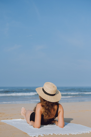Girl in a straw hat sunbathing sitting on the beach and looking at the oceanの写真素材