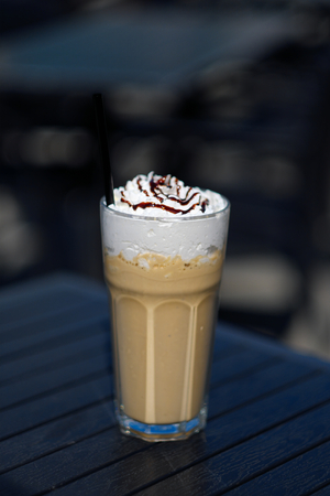 latte macchiato coffee with cream in tall glass with straws on tableの写真素材