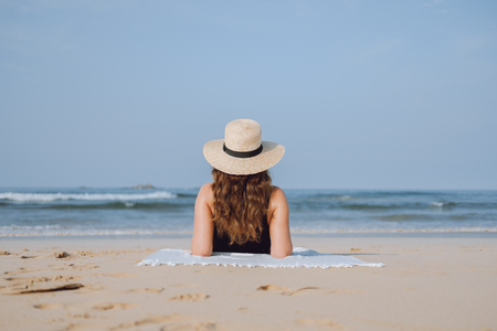 Girl in a straw hat sunbathing sitting on the beach and looking at the oceanの写真素材