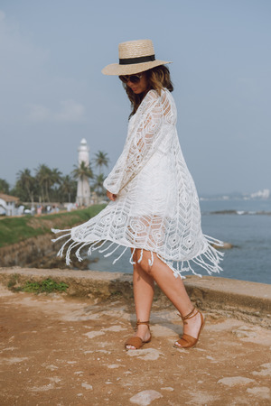 Girl in a hat in a light white clothing waving in the wind whirls around the oceanの写真素材