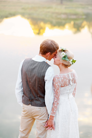 Bride and groom look at each other against the background of the lake. Bride in white dress and wreath on headの写真素材