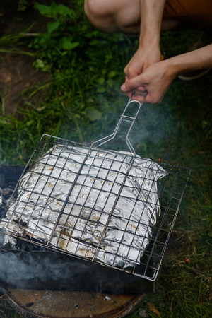 Man fry fish in a foil on a grill in the open airの写真素材