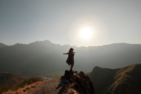 A beautiful girl in a flying dress is standing on a cliff overlooking the mountains. Military-Georgian roadの写真素材