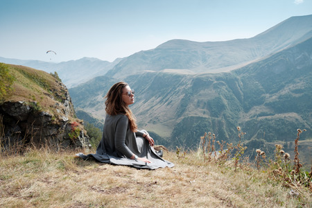 Beautiful young woman in a long dress sits on a background of mountains. Caucasus Mountains in...
