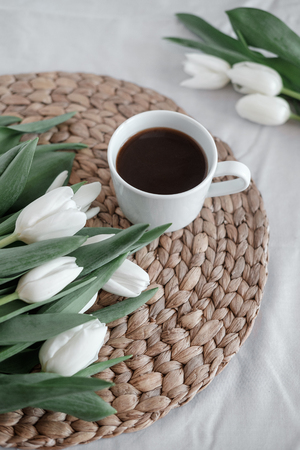 A bouquet of white tulips and a cup of coffee on a white tableの写真素材
