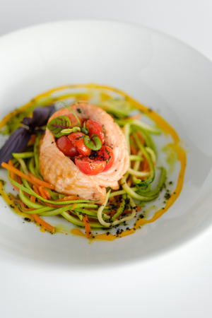 Salmon with spaghetti from courgettes and carrots in a white plateの写真素材