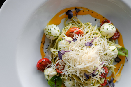 Spaghetti with basil and mozzarella cheese in a white plateの写真素材