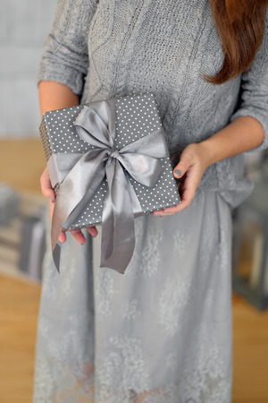 Young woman in a gray sweater opens a box with a Christmas presentの写真素材