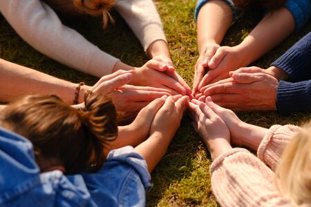 Close up of hands of people sitting outdoors on green grass after doing yoga