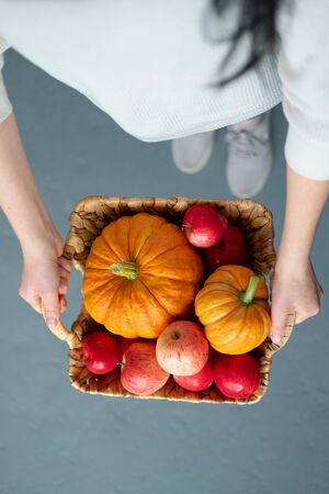 A young girl holds in her hands a wicker basket with red apples and pumpkins. Harvest concept. Early autumn. Thanksgiving Day.の写真素材