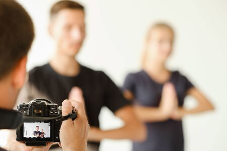 The photographer takes pictures of a young couple in sportswear doing yoga and holding hands in the namaste position.の写真素材