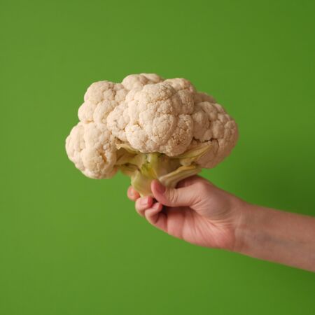 The concept of healthy proper nutrition - cauliflower in a female hand on a green background. Ripe fresh cabbage.の写真素材