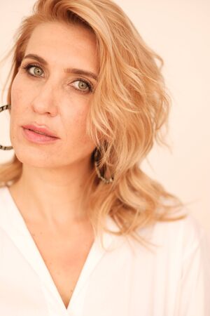 A beautiful blonde with green eyes in a white dress is looking at the camera. Closeup woman portrait