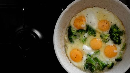 tasty fried eggs with broccoli in a pan is cooked on an gas stove. breakfast concept. view from...