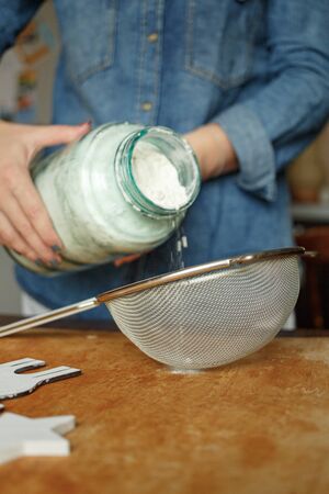 Girl pouring flour from a large glass jar into a sieve. The process of making gingerbread Christmas tree cookiesの写真素材