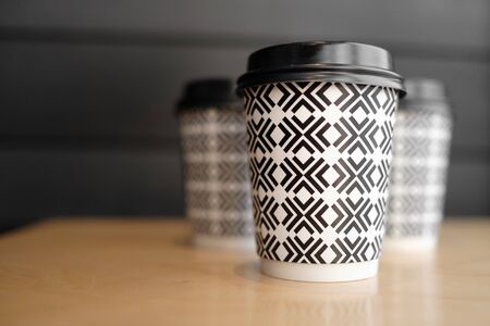three paper cups with a black and white pattern stand on a wooden table. side view. takeaway coffee conceptの写真素材