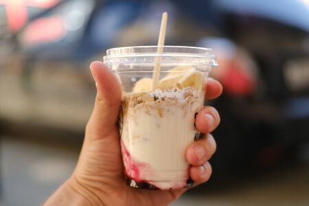 breakfast with you. granola with yogurt in a plastic cup in a hand. takeaway food conceptの写真素材
