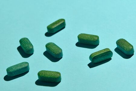 Heap of medicine tablets and pills on blue background. nutrition supplements, green vitamin pills. Healthcare or medicament addiction concept.の写真素材