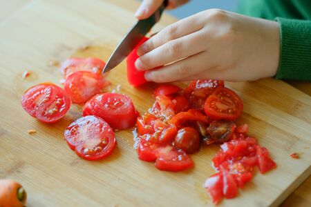 A young girl in a green sweater slices tomatoes to make a salad. The concept of healthy proper...