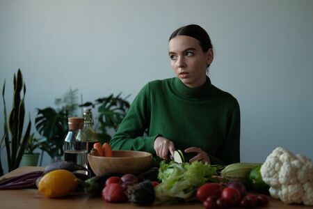 A girl in a green sweater cuts a zucchini knife with rings and slices on a wooden cutting board. On...
