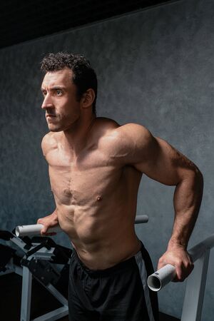 Muscular bodybuilder working out in gym doing exercises on parallel bars. Athlitic male naked torsoの写真素材