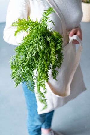Hands holding reusable eco friendly canvas bag with fresh carrots and greenery. Zero waste grocery shopping. Ban plastic.の写真素材