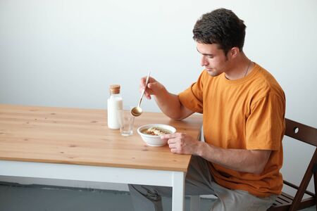 A young guy in a yellow T-shirt is having breakfast. The guy holds a spoon in his hand. Healthy eating conceptの写真素材