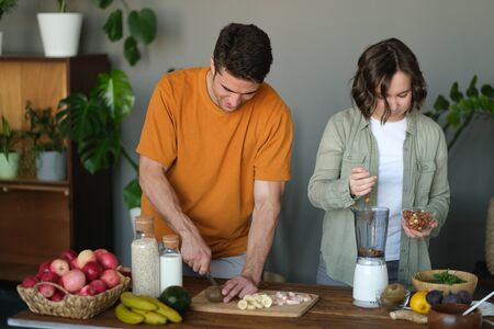 Young married couple makes a smoothie: a guy cuts kiwi, a girl grinds nuts in a blender. Concept of...