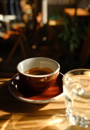 black coffee in a cup and a transparent glass with water on a wooden background. glare in the sun. beautiful light. alternative coffee.uprightの写真素材