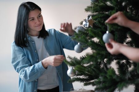 Female hands decorate the Christmas tree. In the background in bokeh a young girl with black hair...