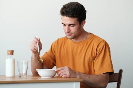 A young guy in a yellow T-shirt is having breakfast. The guy holds a spoon in his hand to start breakfast. Healthy eating conceptの写真素材
