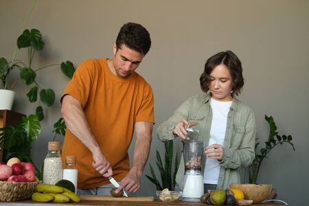 Young married couple makes a smoothie: a guy cuts kiwi, a girl grinds nuts in a blender. Concept of...