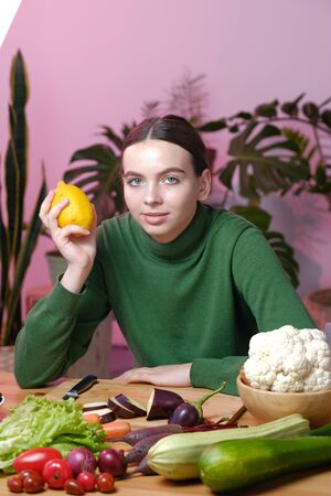A young girl in a green sweater holds a lemon in her hand. On the table are many different vegetables and fruits, the concept of veganism, vegetarianism, healthy eating, diet.の写真素材