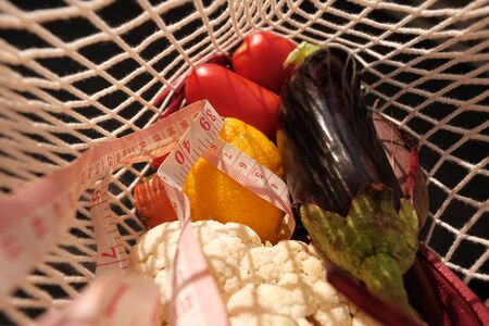 Closeup vegetables, fruits and waist measuring tape in a rope bag. Healthy eating and dieting...