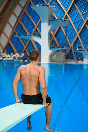 young athlete swimmer sitting on the edge of a platform for diving in an indoor pool. Swimmer mentally preparing for the upcoming competition. Professional Sprat Conceptの写真素材