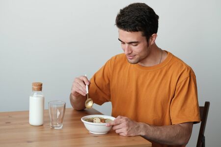 A young guy in a yellow T-shirt is having breakfast. The guy holds a spoon in his hand to start...