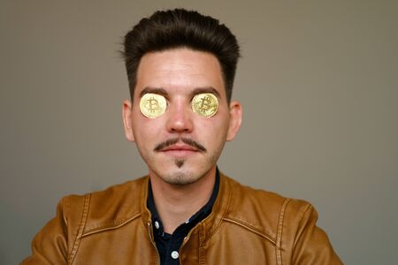 Young man holds golden bitcoin in eye sockets. Crypto currency Coins - Bitcoin
