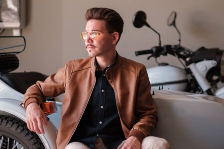 guy in stylish glasses on the background of motorcycles in the garage. Casual style. portrait of a successful man. fashionable and confidentの写真素材