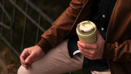 Young guy holds a cigarette and coffee in an eco mug.の写真素材