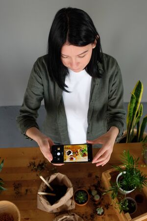 young girl photographs home plants on the phone. eco blogger. ecology. hobby. concern for the...
