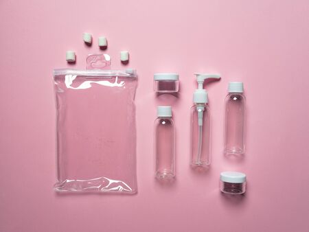 Travel set of bottles, jars and a transparent cosmetic bag on a pink background. View from above