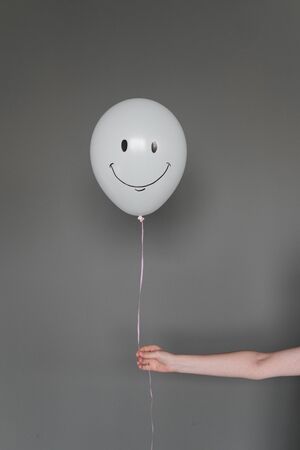 Balloon with a smile emotion in a human hand on a gray background. Emotion concept