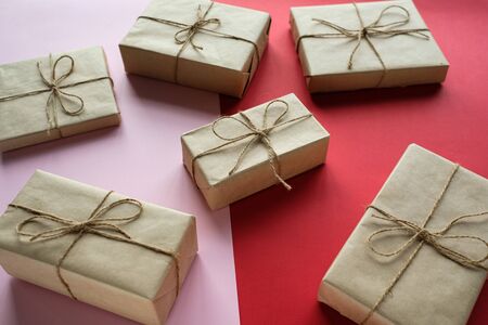 Christmas gifts in gift boxes wrapped in kraft paper and tied with twine lie on a red-pink...